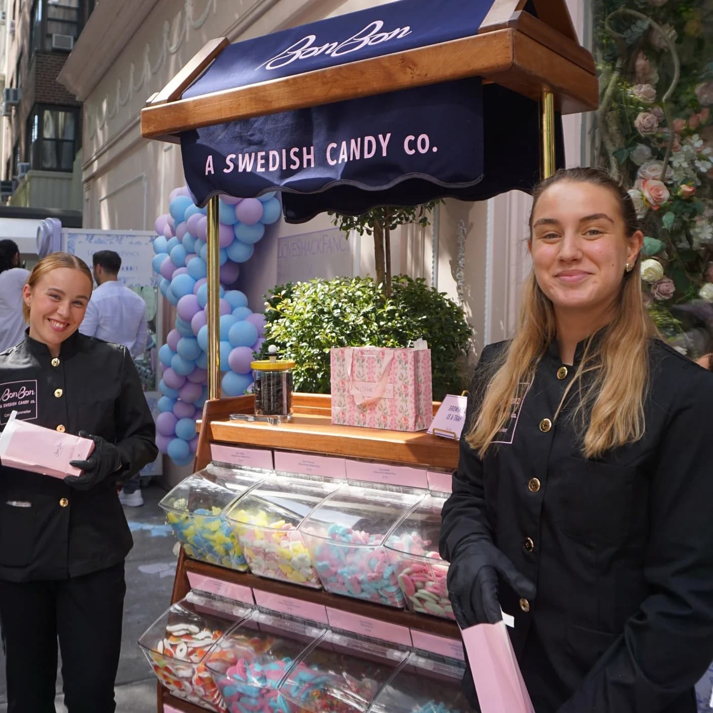 Two attendants beside a BonBon Swedish candy cart filled with colorful sweets