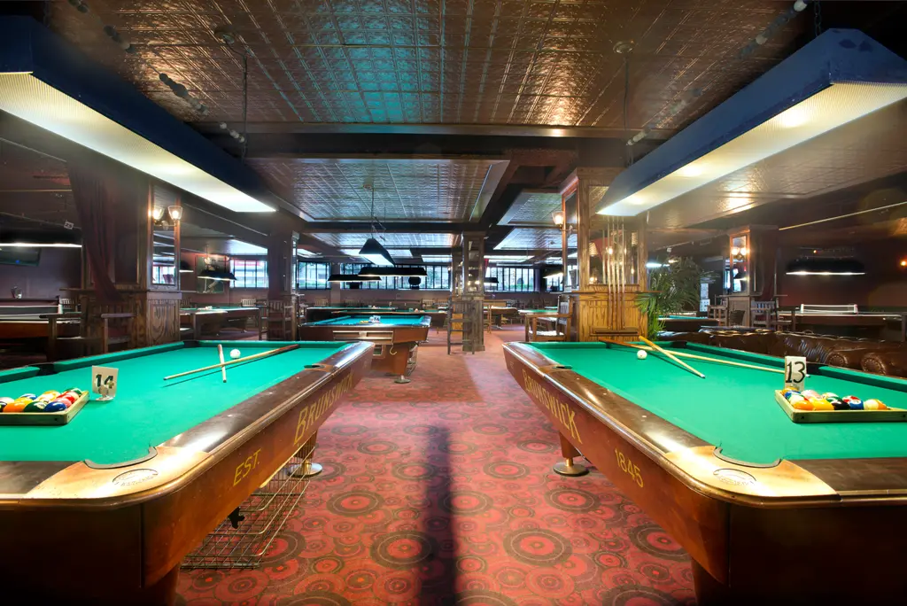 looking down the pool hall between the rows of pool tables