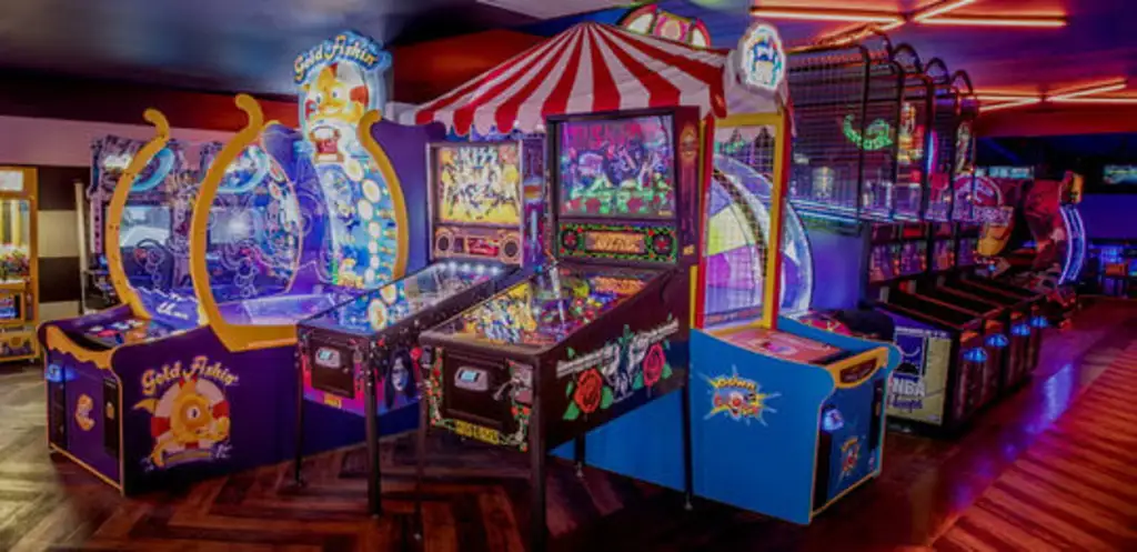An exciting arcade featuring a variety of colorful pinball machines and carnival-themed games, all illuminated by vibrant neon lights, creating a lively ambiance.