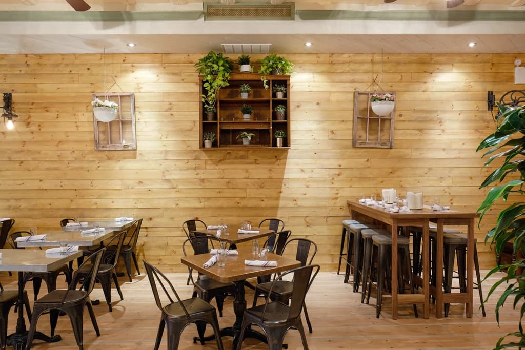 Cozy restaurant interior with wooden walls, metal chairs, and plants, creating a warm and inviting atmosphere.
