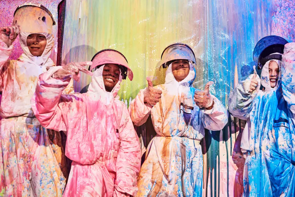people in white suites, coverd in paint, smiling at the camera