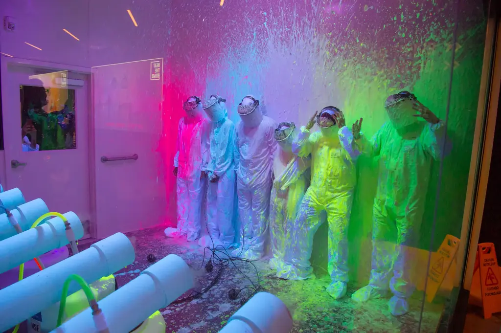 a line of people in white suits and face shields with paint being shot at them