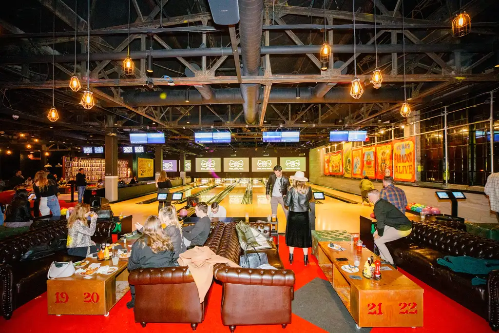 People enjoying a lively night out at a bowling alley, with leather seating, vibrant decor, and multiple bowling lanes.