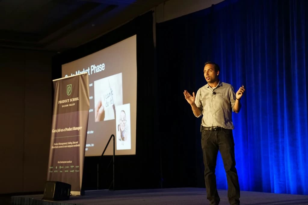 a person standing on a stage and presenting with a screen behind them