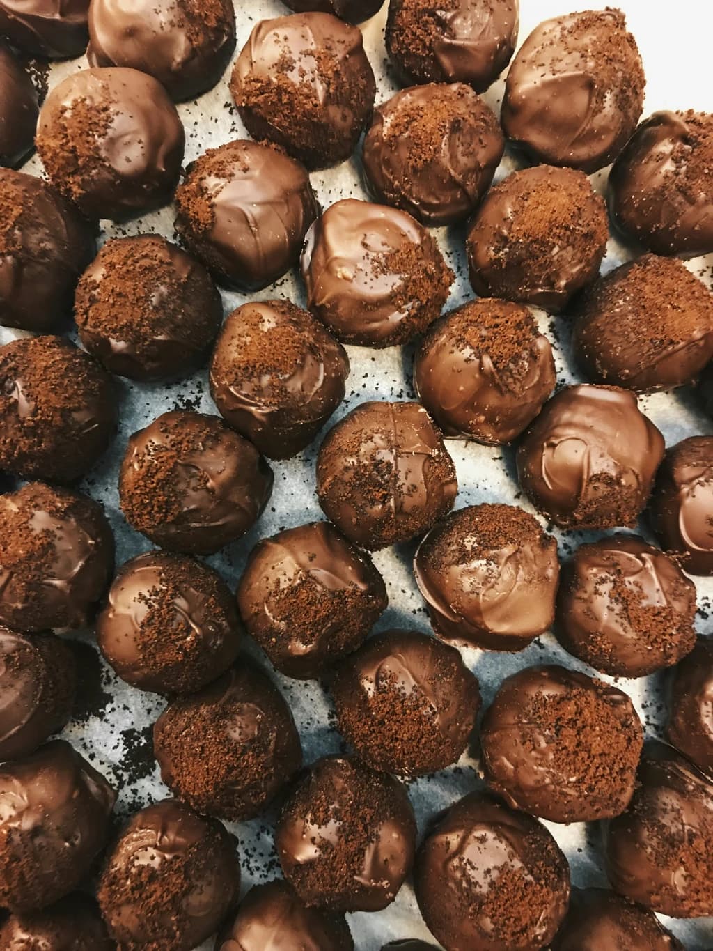 Rows of freshly made chocolate truffles coated with a glossy chocolate layer and sprinkled with cocoa crumbs.