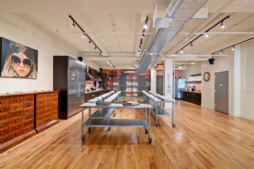 A spacious, well-lit kitchen studio with wooden floors, equipped for cooking classes and culinary events.