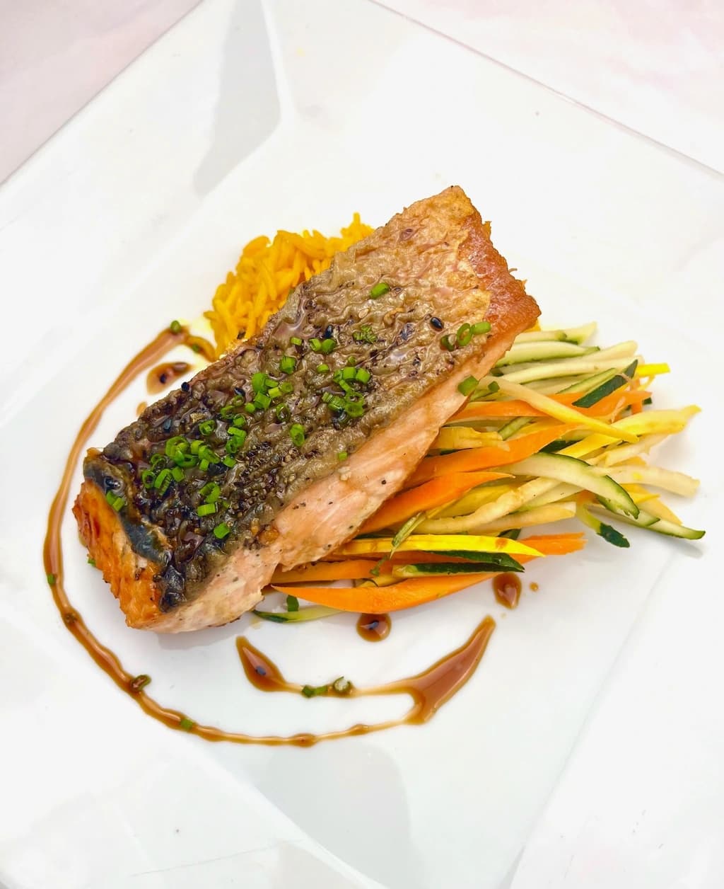 A beautifully plated salmon dish with crispy skin, resting on a bed of julienned vegetables, drizzled with sauce.