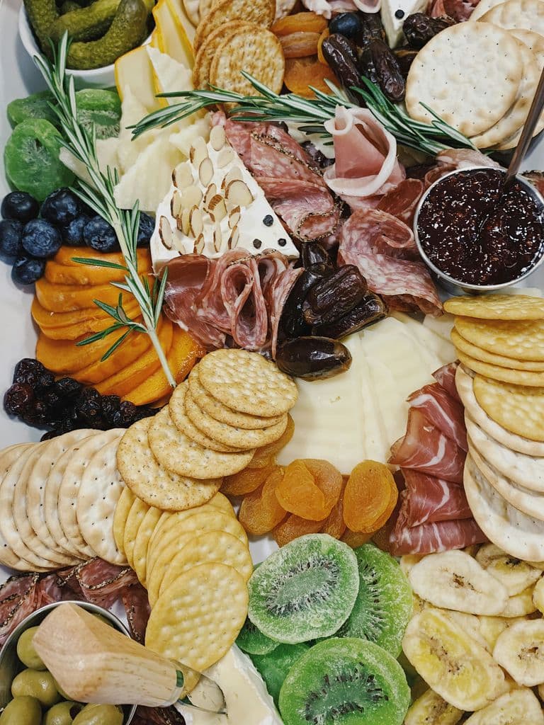Close-up of a vibrant charcuterie board with assorted crackers, cured meats, cheeses, dried fruits, pickles, fresh berries, nuts, and a small bowl of jam.