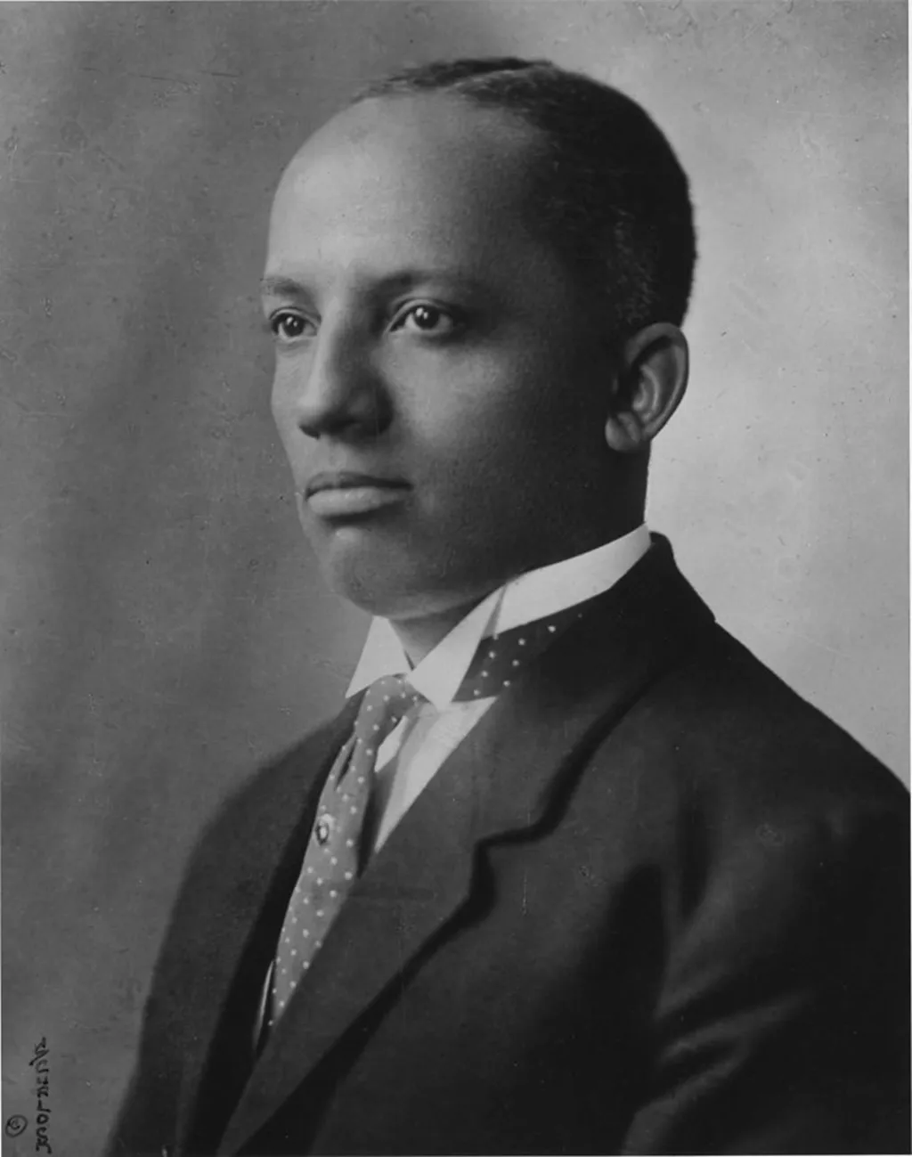 A black-and-white portrait of a man in formal attire looking off to the side with a serious expression.