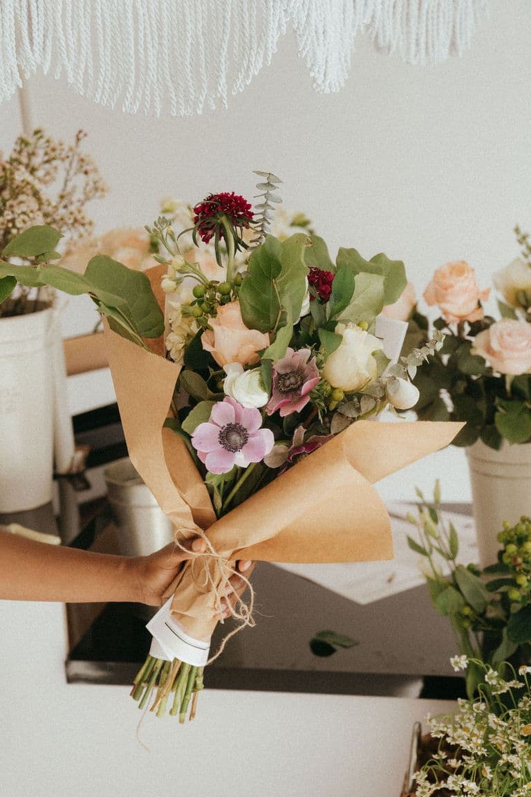Hand holding a wrapped bouquet of mixed seasonal flowers at a flower bar setup.