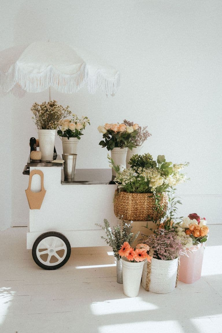 Minimal white flower cart with soft-toned florals arranged in buckets and baskets, bright natural light.