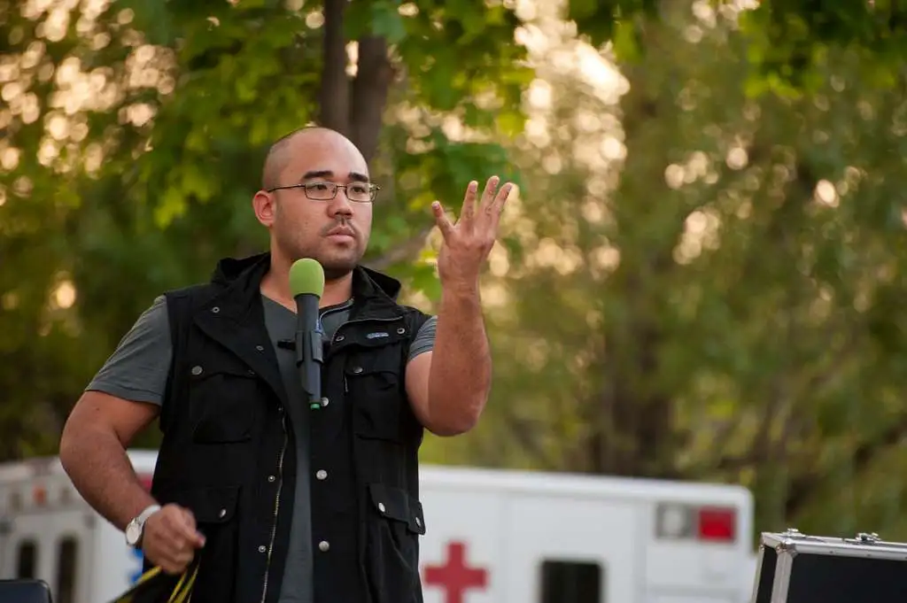 a man standing infront of a microphone, doing a trick with his hands
