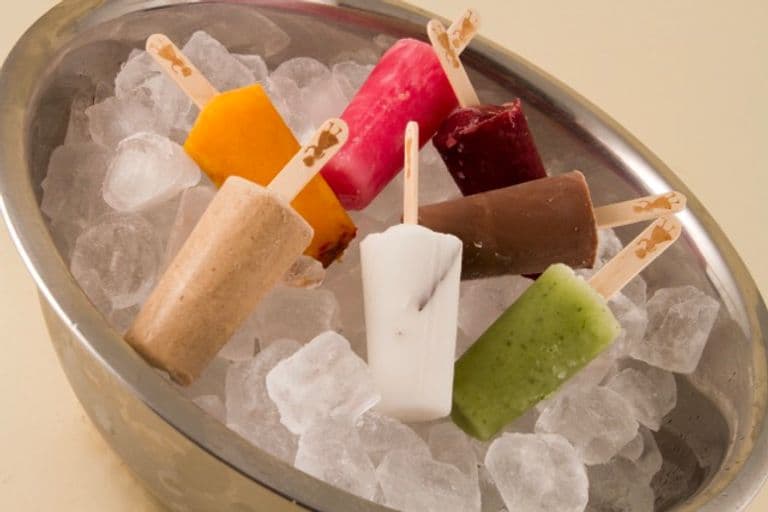 Assorted mini paletas in bright flavors displayed on ice in a metal bowl, showing the colorful variety available.