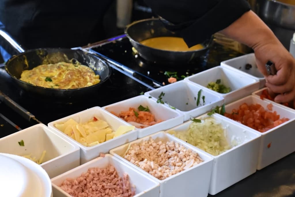 A chef preparing an omelette at an omelette bar, with various toppings in small containers.