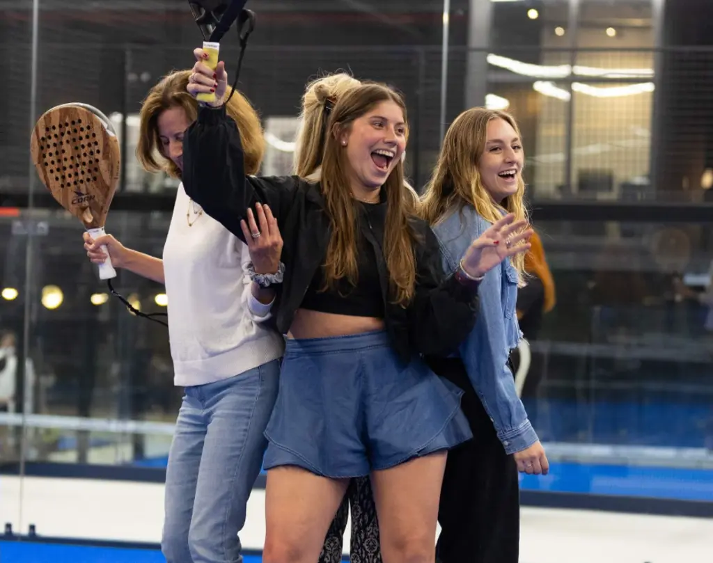 Group of young women enjoying a game of padel, holding rackets and cheering energetically on the court.