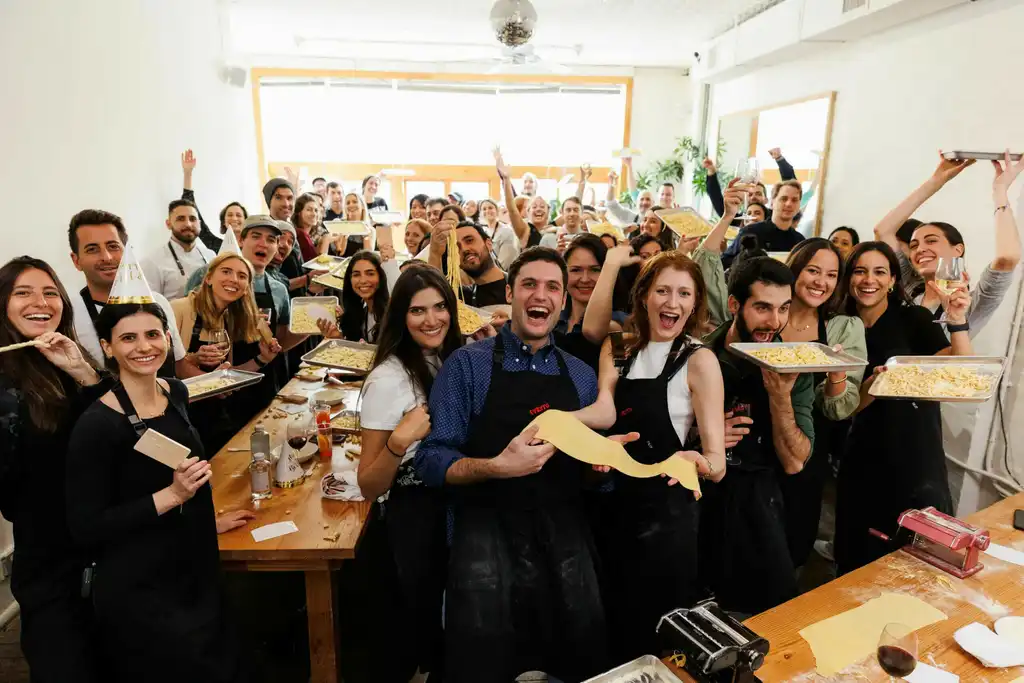 a large group of people all facing the camera, smiling, and showing the pasta they made