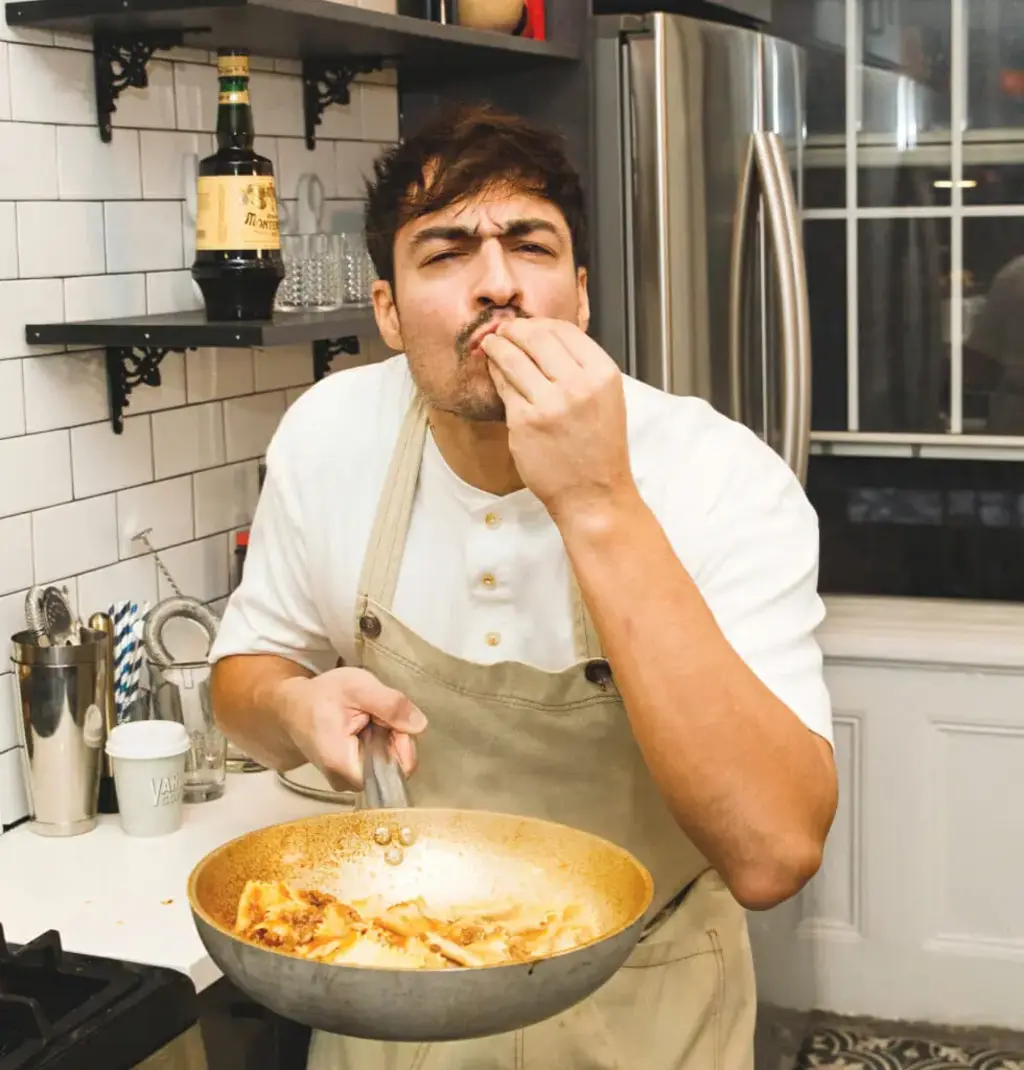 a man holding up a dish with freshly cooked pasta in it and giving the chef's kiss
