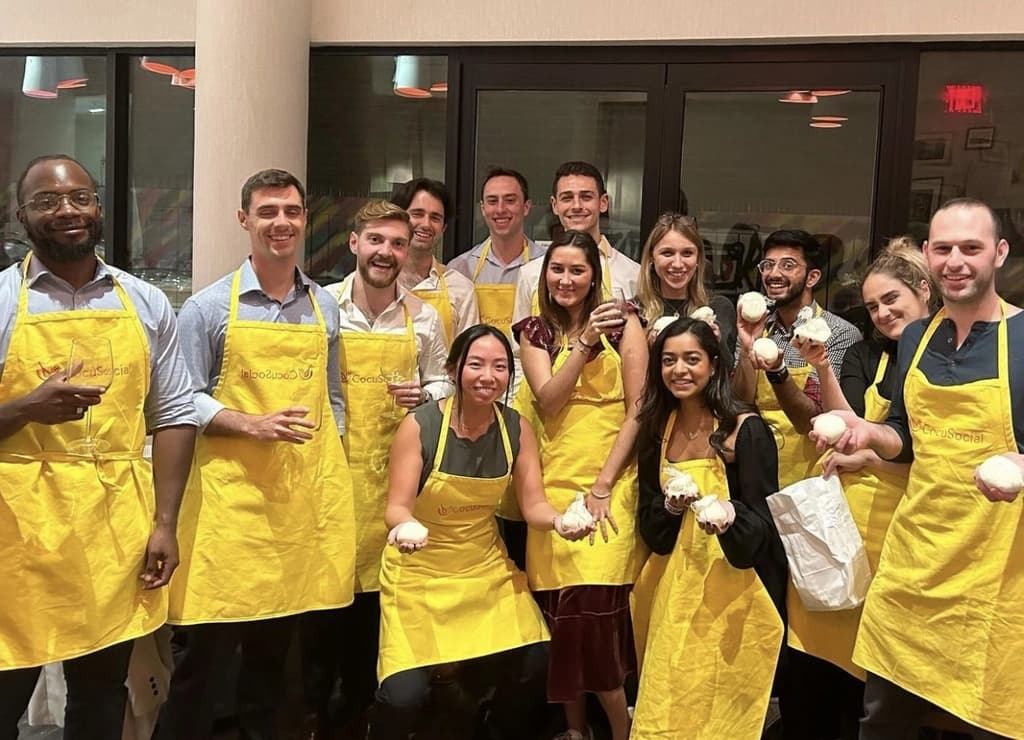 A group of smiling participants wearing yellow aprons, proudly displaying their culinary creations during a cooking class or social event.