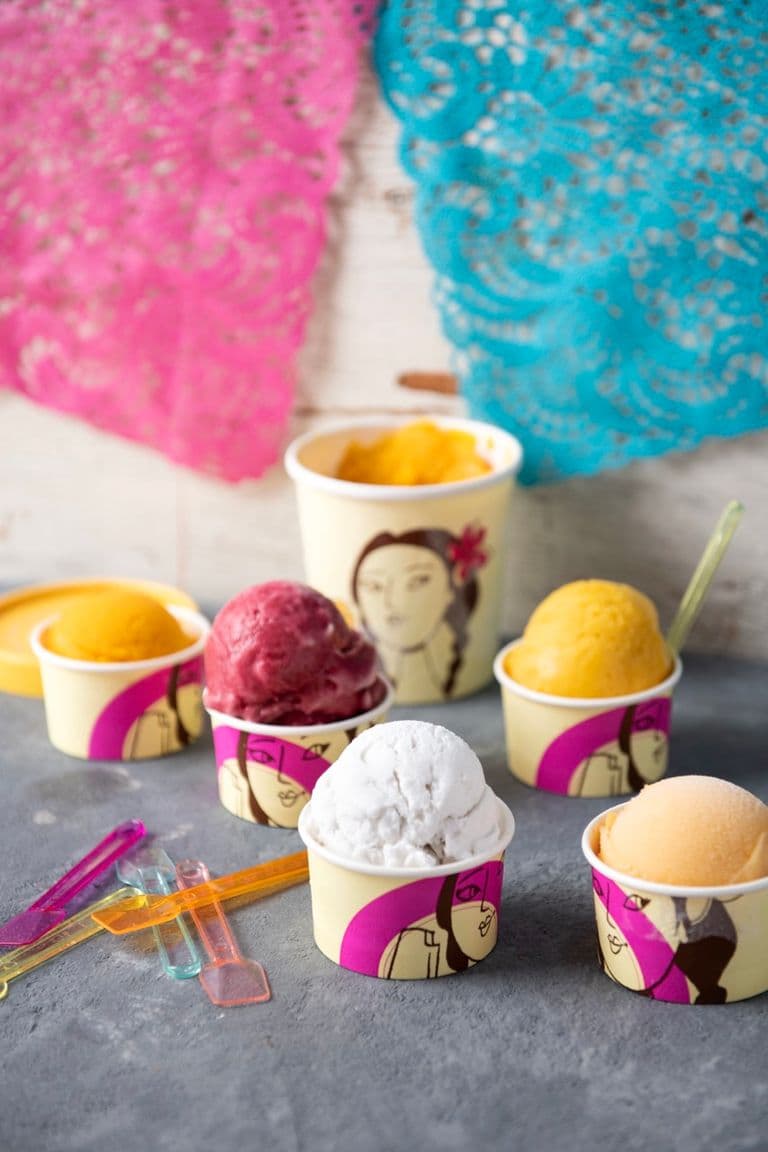 Colorful scoops of ice cream in small cups with plastic spoons, arranged on a table with festive decorations.