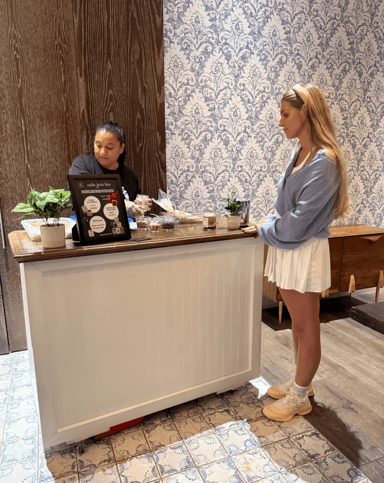 Guest ordering at a dessert bar with a cake pop and cupcake topping station set up on a mobile counter.