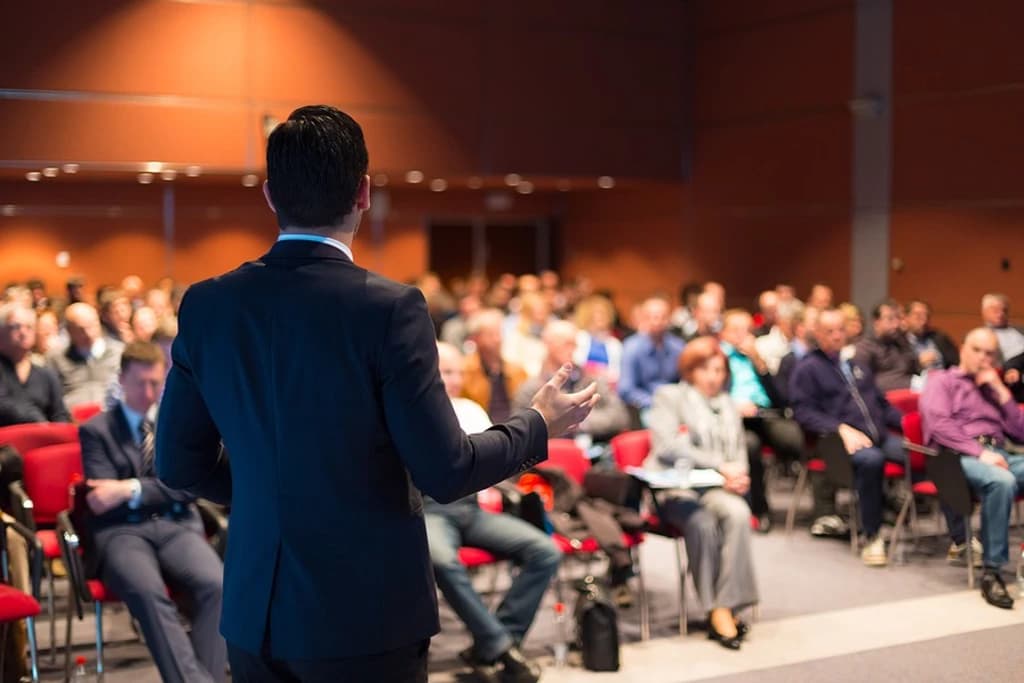 the back of a speaker on stage with an audience in front of them