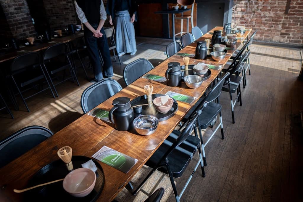Long wooden tables set up for a tea ceremony, with traditional tea-making utensils arranged neatly for participants.