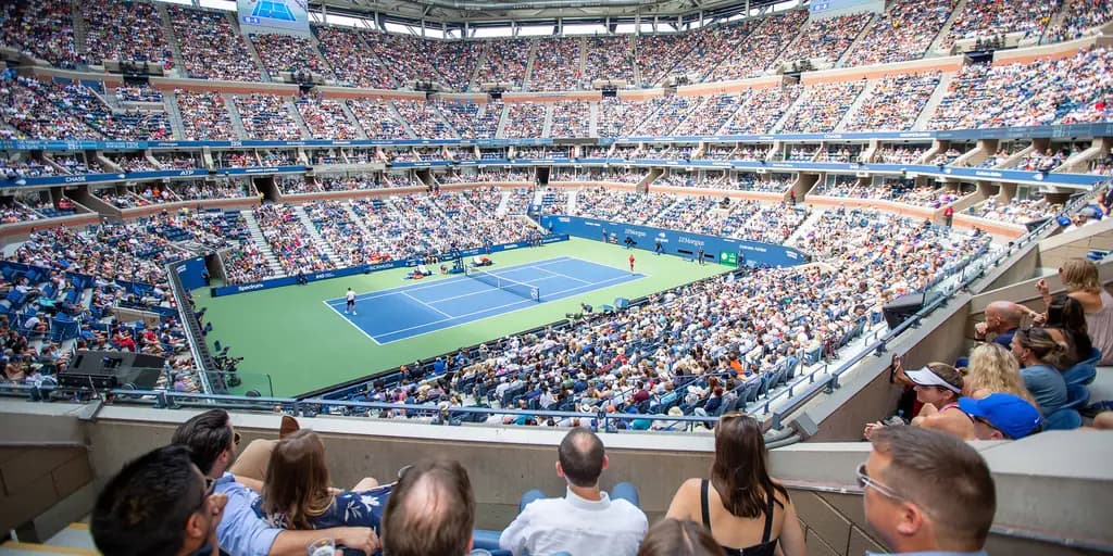 Packed tennis stadium with fans watching a match, featuring a large central court and tiered seating filled with spectators.