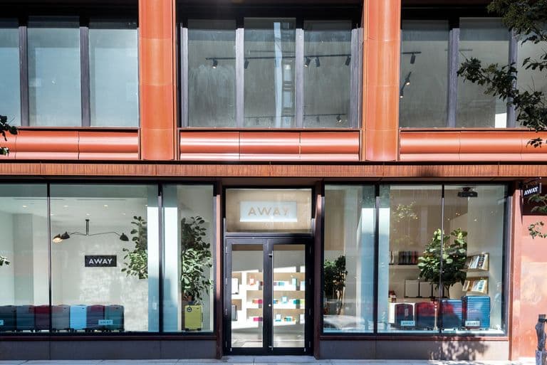 Street view of the Away store with floor-to-ceiling windows and suitcases visible through the glass.