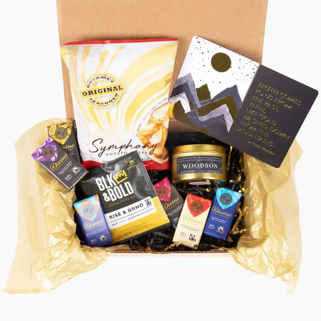 A gift box containing snacks, chocolate bars, coffee, a candle, and a decorative card on golden tissue paper.