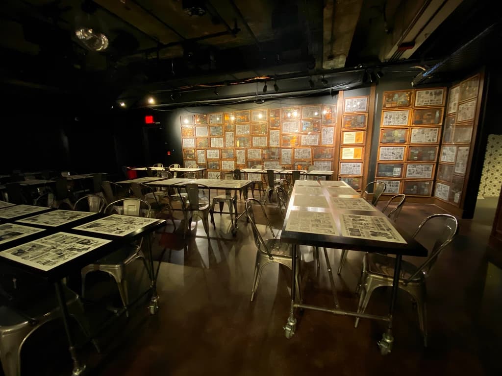 Dining area with tables and chairs in a dimly lit setting, featuring comic strip decorations on the walls.