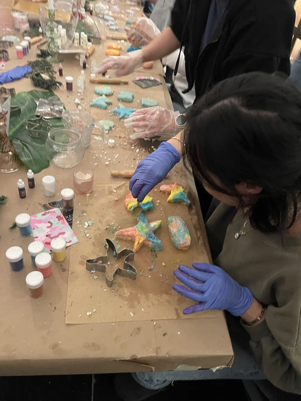 A woman in a white blouse stands behind a table set up for a cookie decorating workshop, featuring cookie cutters, molds, and fall-themed decorations.