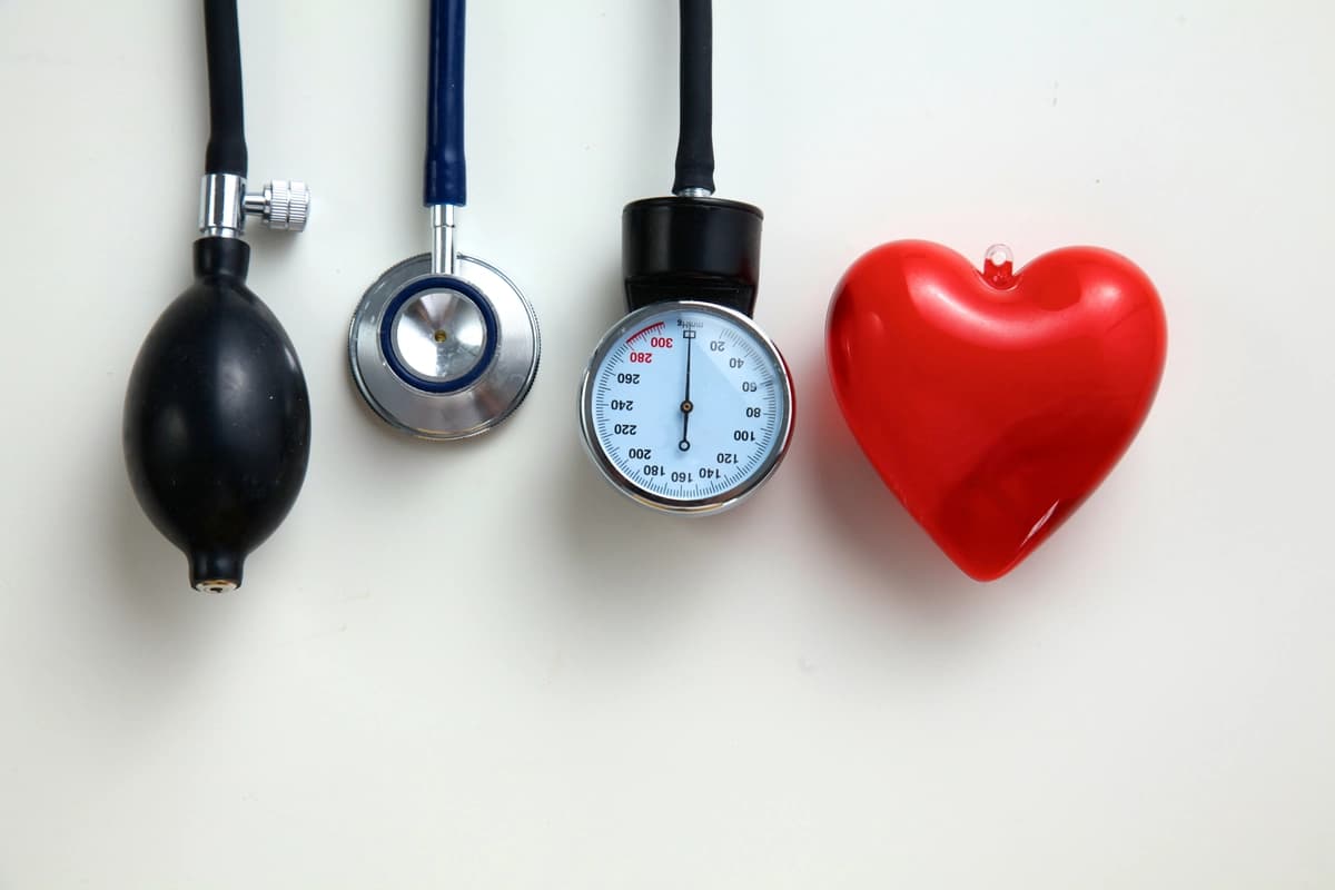 Blood pressure cuff, stethoscope, sphygmomanometer, and a red heart model on a white background.