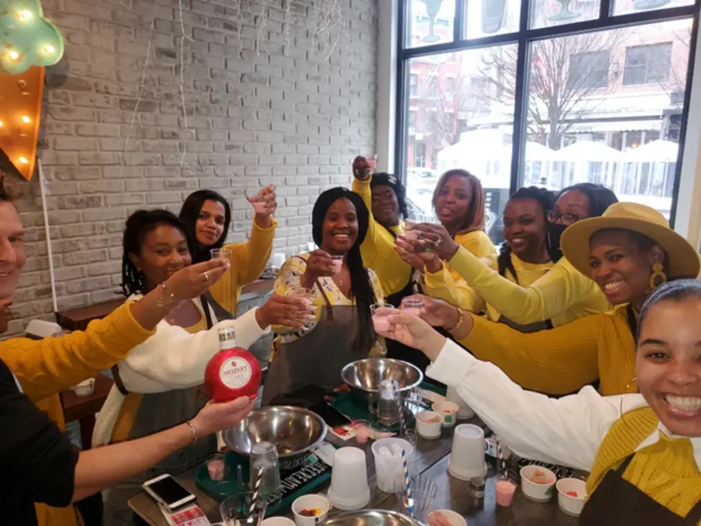 Participants stand in a kitchen, sampling ingredients and following instructions during a hands-on boozy ice cream-making class.