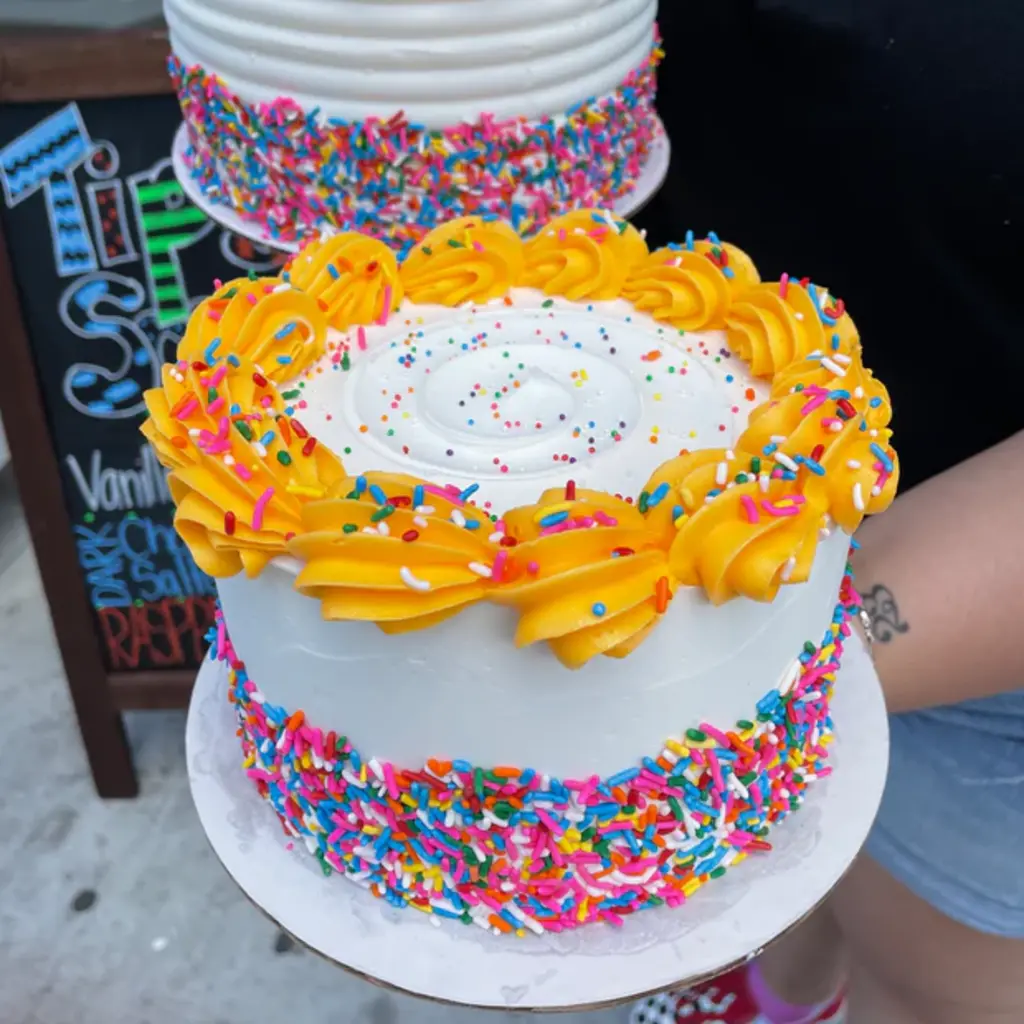 A group of friends sitting around a table at a cake decorating event, smiling and enjoying their time together with drinks in hand.