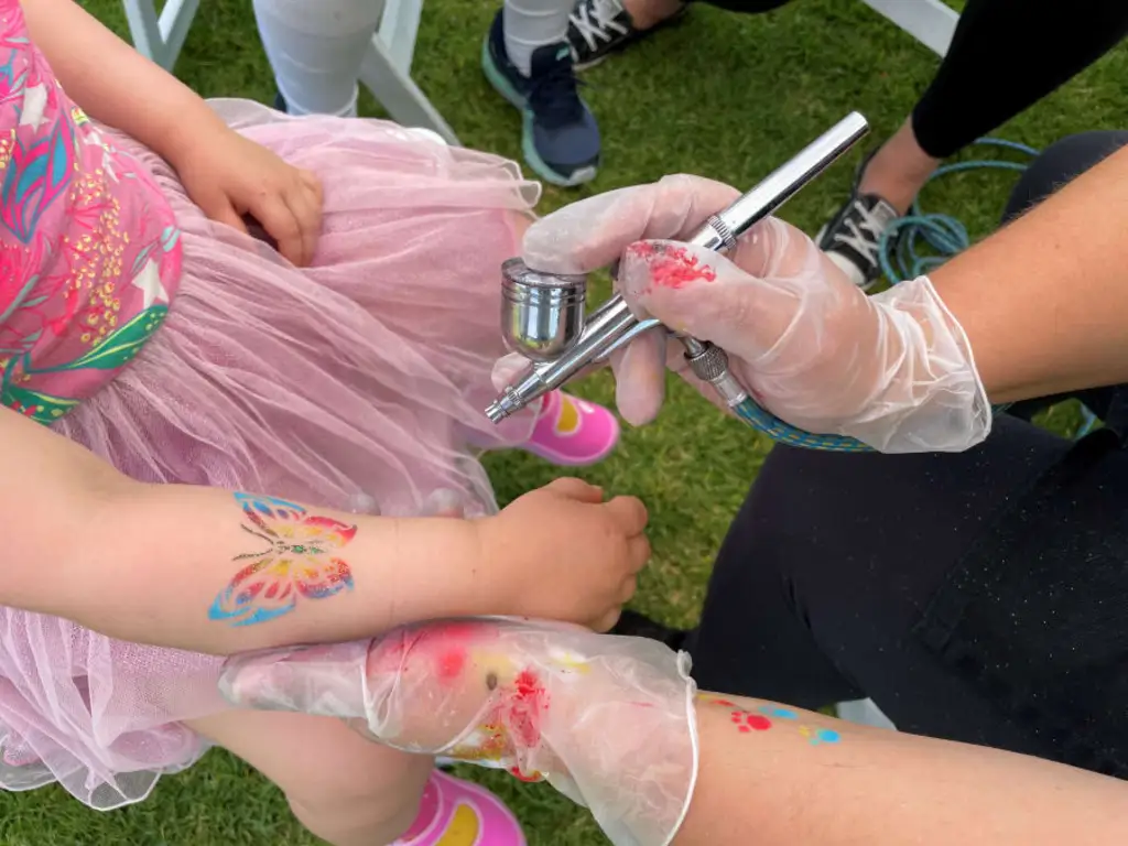 someone giving a child an airbrush butterfly tattoo