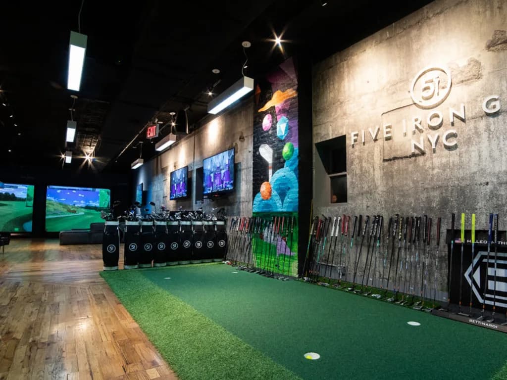 a putting green with holes and clubs around it, and golf simulators in the background