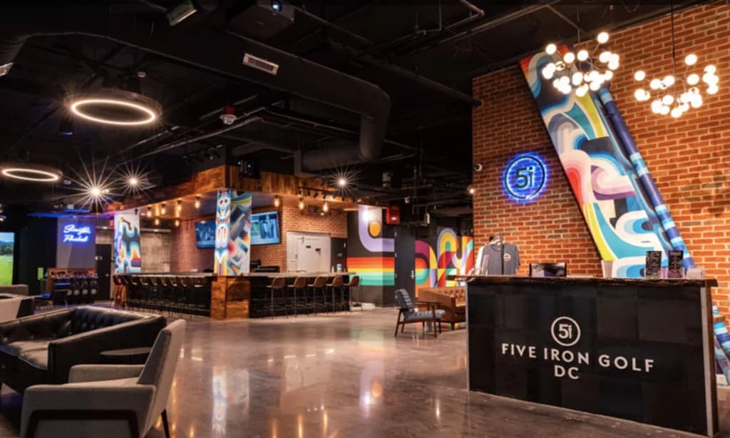 a bar with lights, colorful signage, and golf simulators in the background