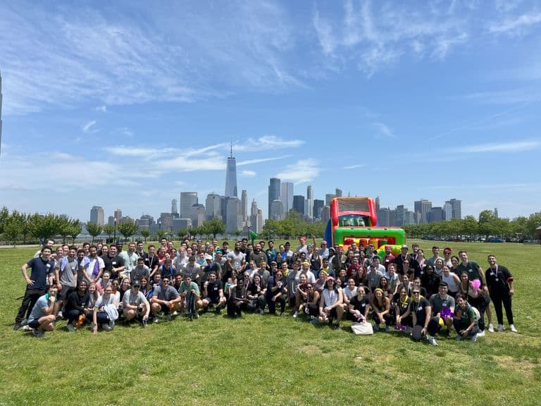 Large group posing in front of a colorful inflatable and the NYC skyline on a clear, sunny day in the park.