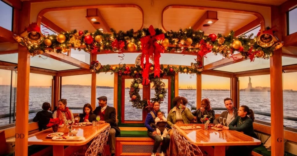 Guests enjoying a cozy, holiday-themed boat cruise with festive decor and the Statue of Liberty in the distance.