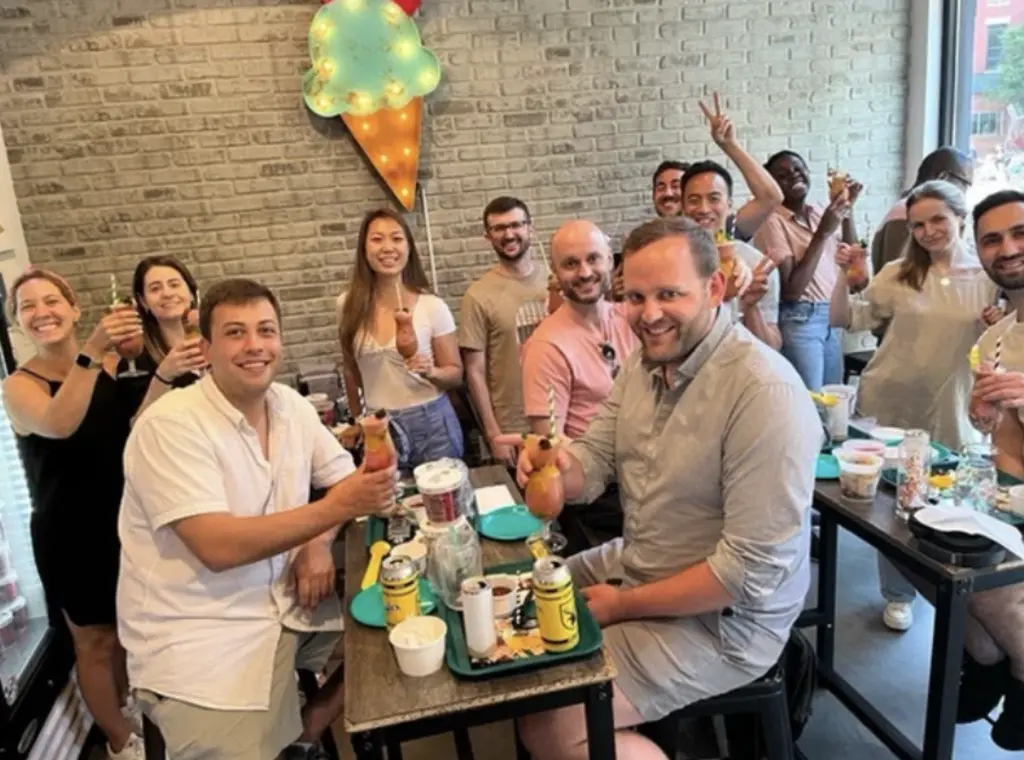 Four friends posing together at an ice cream bar, each holding large decorative ice cream cocktails, seated under a sign that reads 'BARLOUR.'