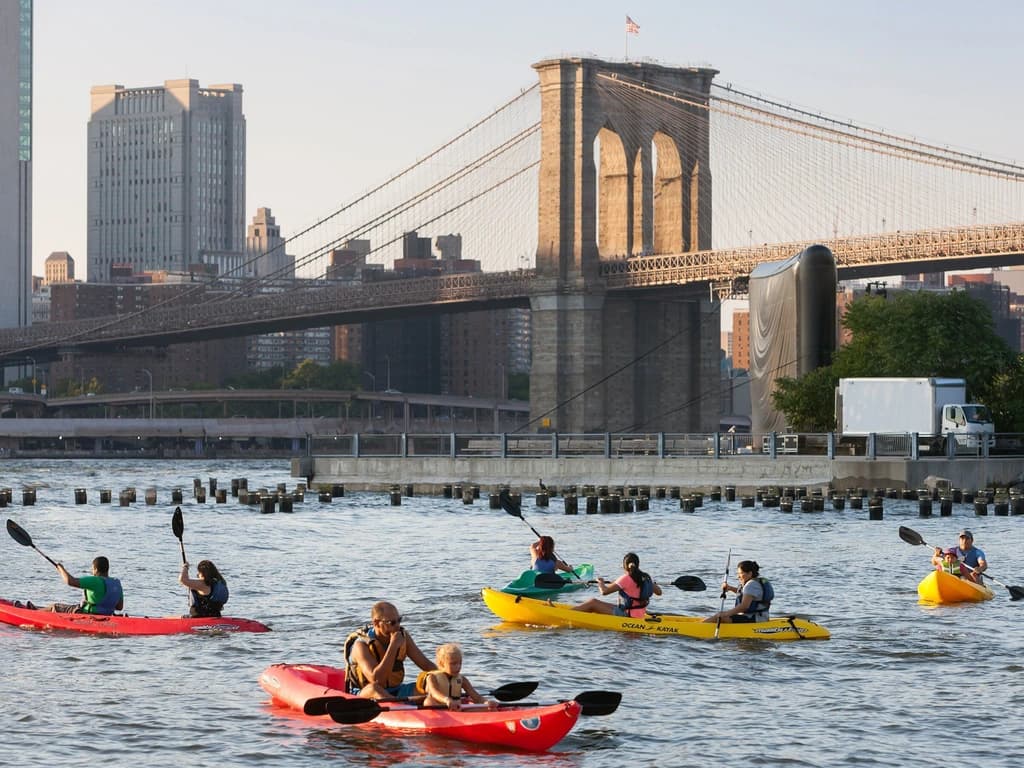 Lots of people kayaking in the Hudson River with the Brooklyn bridge in the background