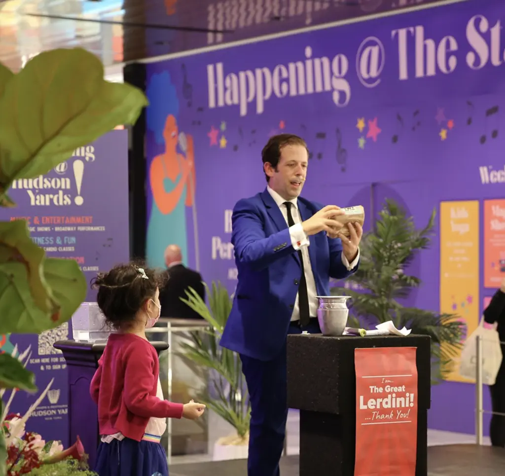 a man doing magic on a stage and a child helping him