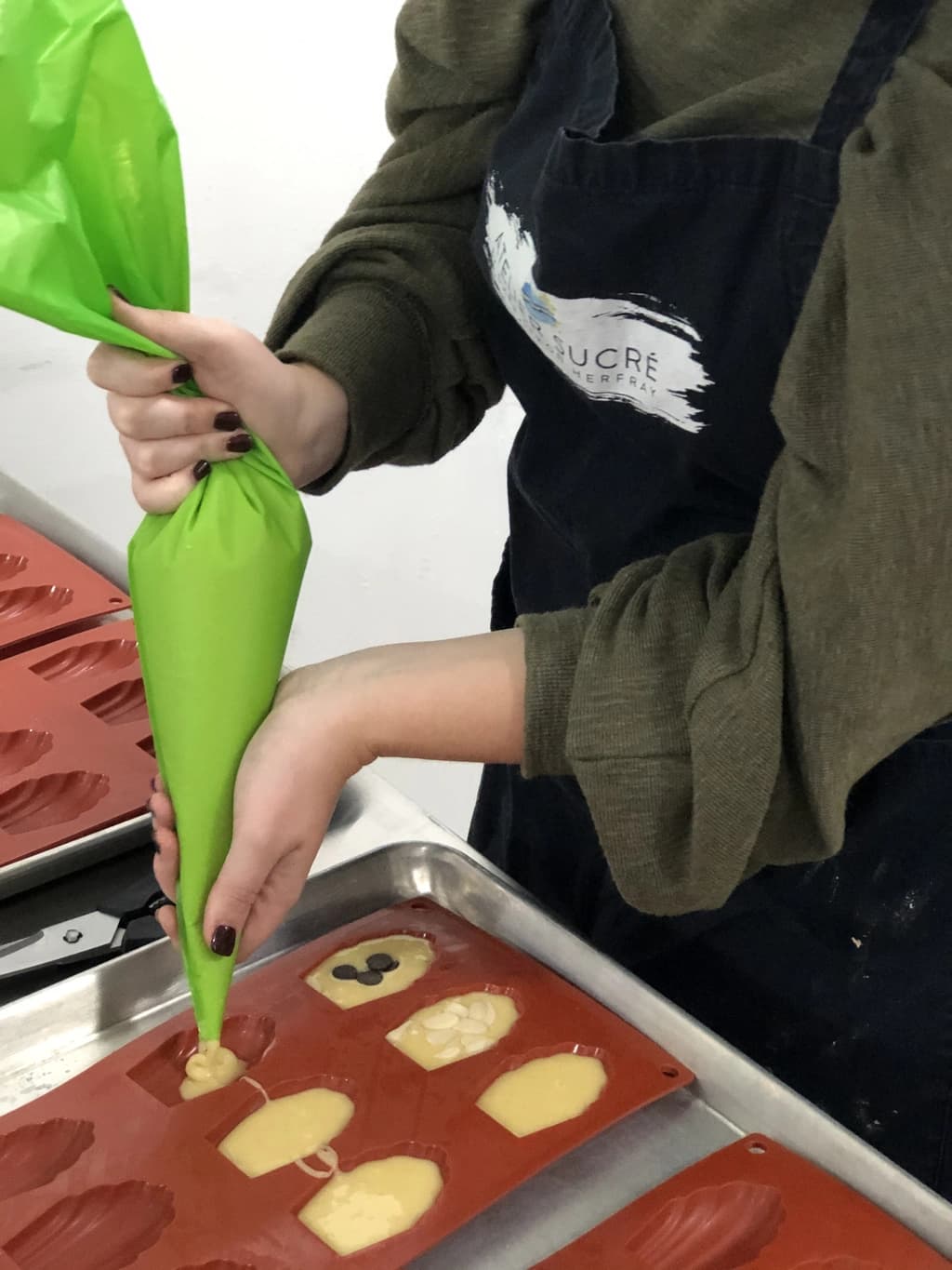 A person in an apron piping batter into silicone molds, preparing decorative chocolate shapes on a baking tray.