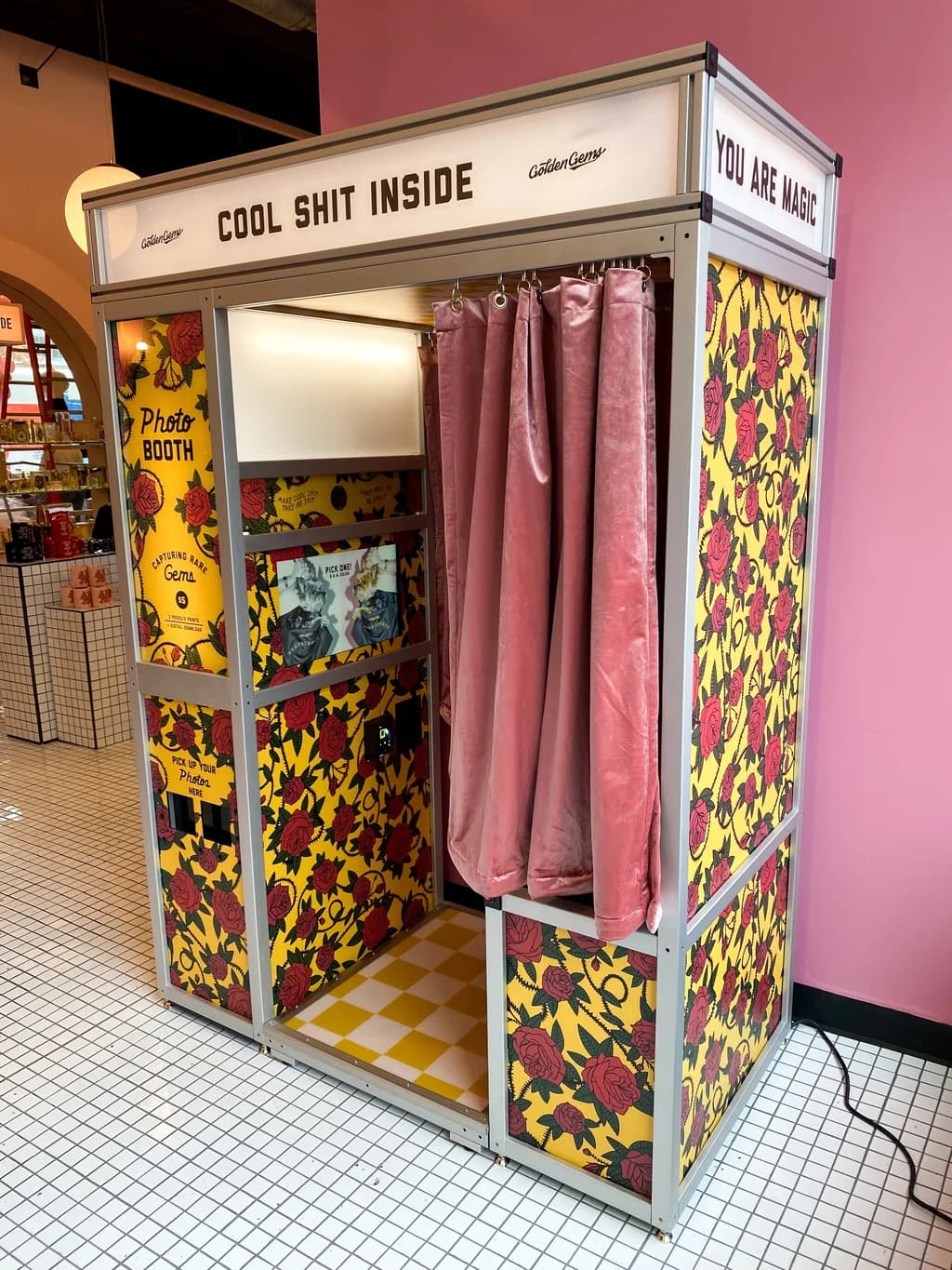 A photo booth with bright floral patterns and pink curtains, featuring the phrase 'Cool Shit Inside.'