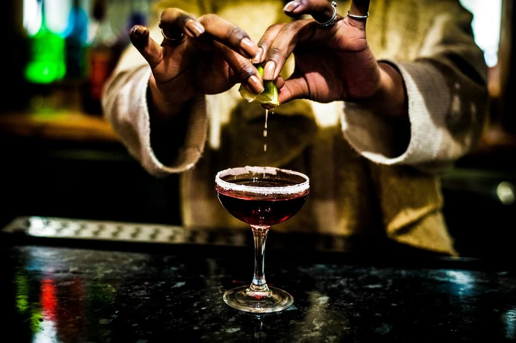 a close up of someon squeezing a lime into a mixed drink