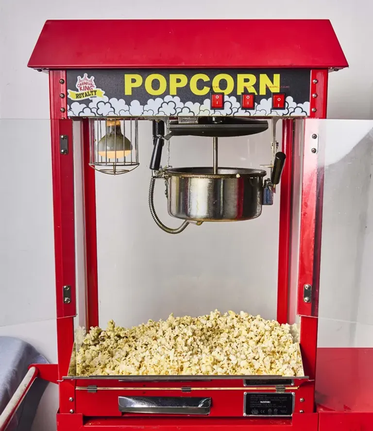 Classic red popcorn machine filled with fresh popcorn, with a metal popping kettle inside.