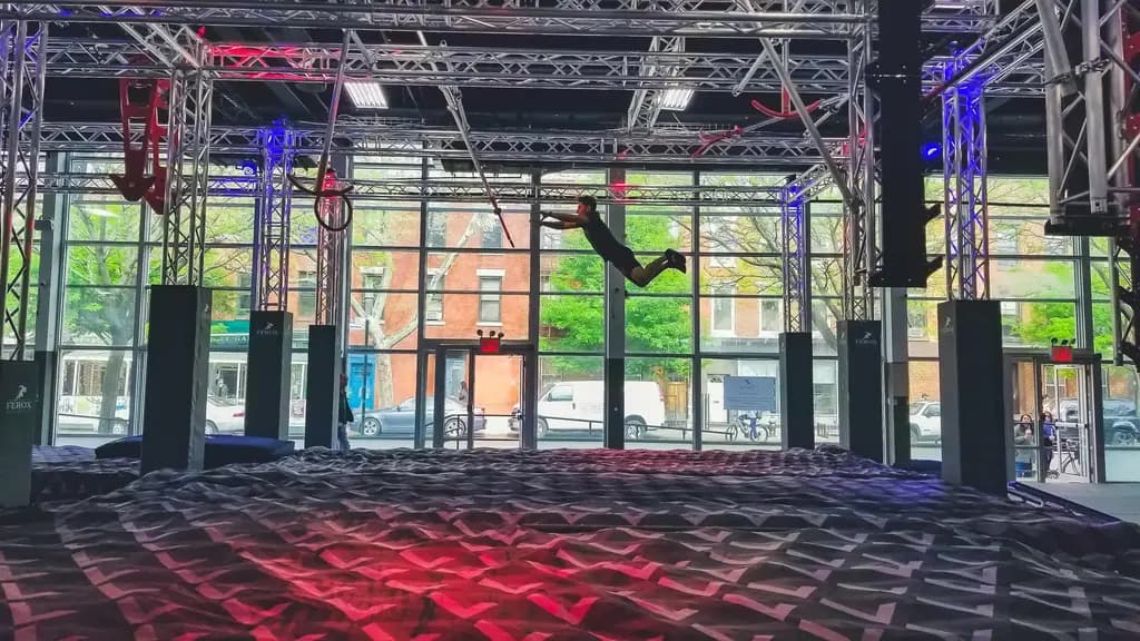 a side view of someone using a trapeze bar over a foam pit at a ninja park