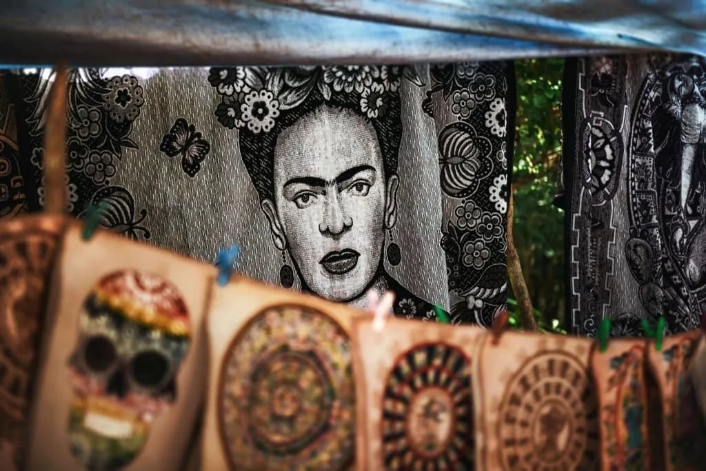 Frida Kahlo tapestry with a detailed, black-and-white portrait, displayed among vibrant, intricately designed fabric artworks at a market.