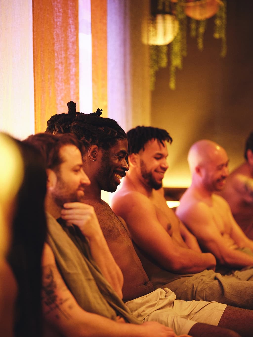 A group of men sitting closely together in a sauna, smiling and enjoying the warmth, with soft, warm lighting creating a cozy atmosphere.
