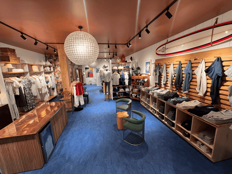 Inviting Faherty store with soft lighting, wooden accents, and colorful spring apparel on racks and shelves; paper lantern lights add a cozy touch.